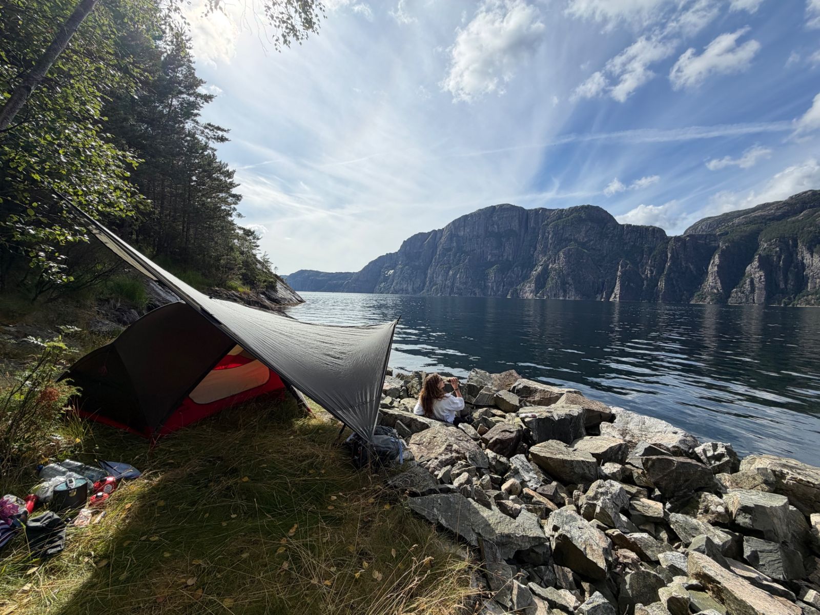Tent with tarp pitched on the shore of Lysefjord, steep cliffs across the water