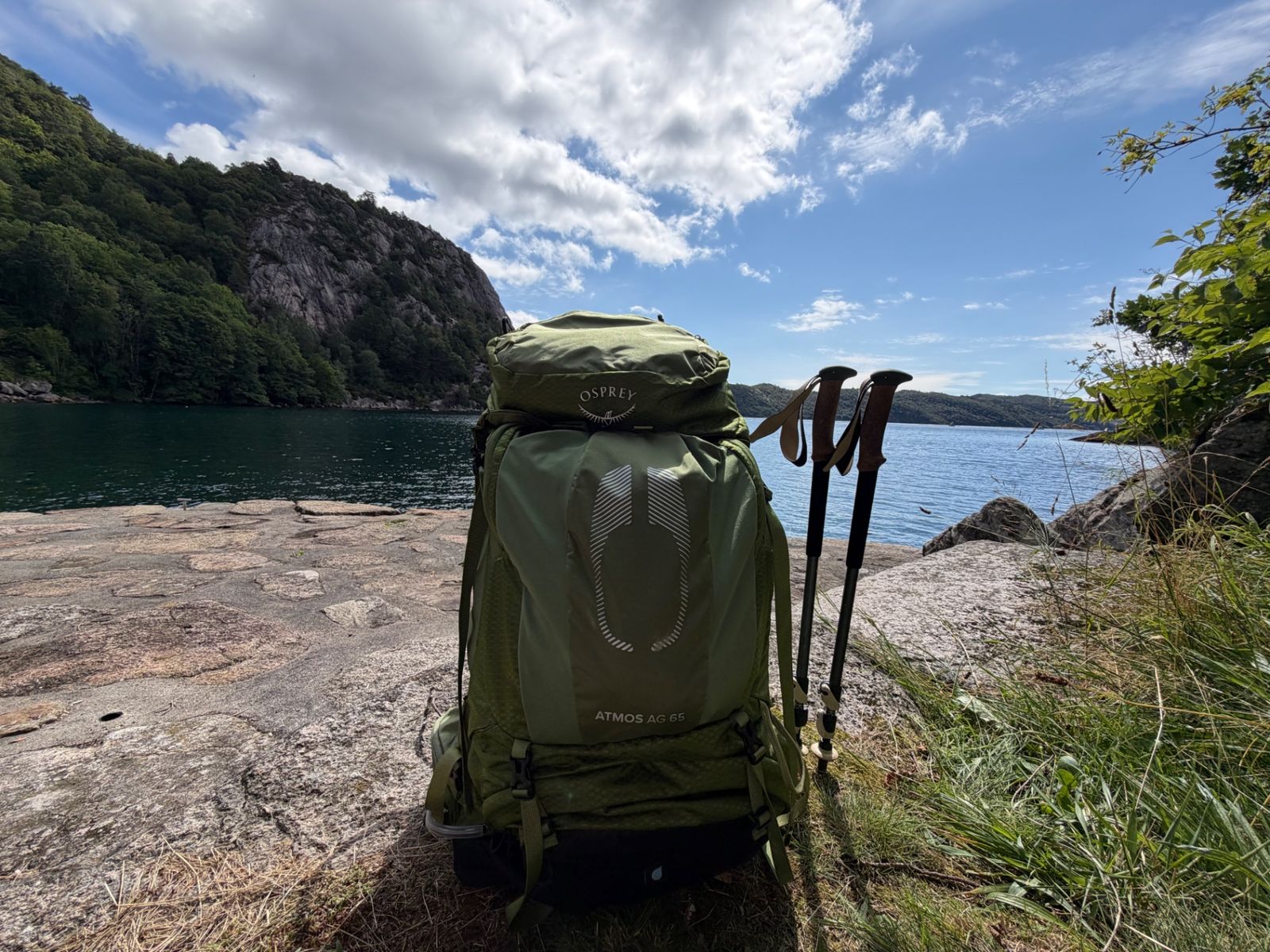 Osprey Atmos AG 65 with the Black Diamond trekking poles on a rock ledge by the fjord
